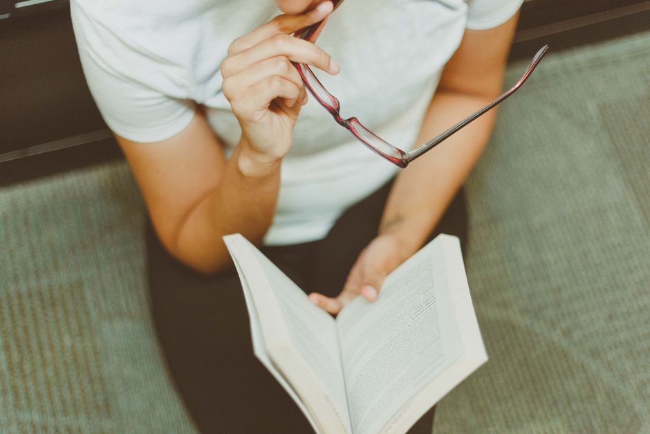 Adult male reading a Bible while seated on a comfortable chair indoors.
