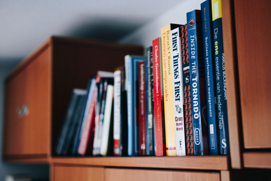 Close-up of hands holding a stack of colorful books in natural light.