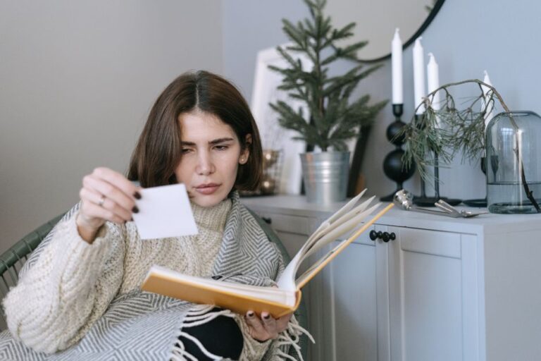 A woman examines a photograph while sitting in a cozy indoor space, surrounded by decor.