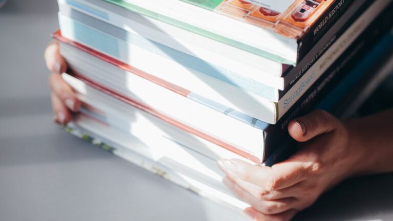 Close-up of hands holding a stack of colorful books in natural light.