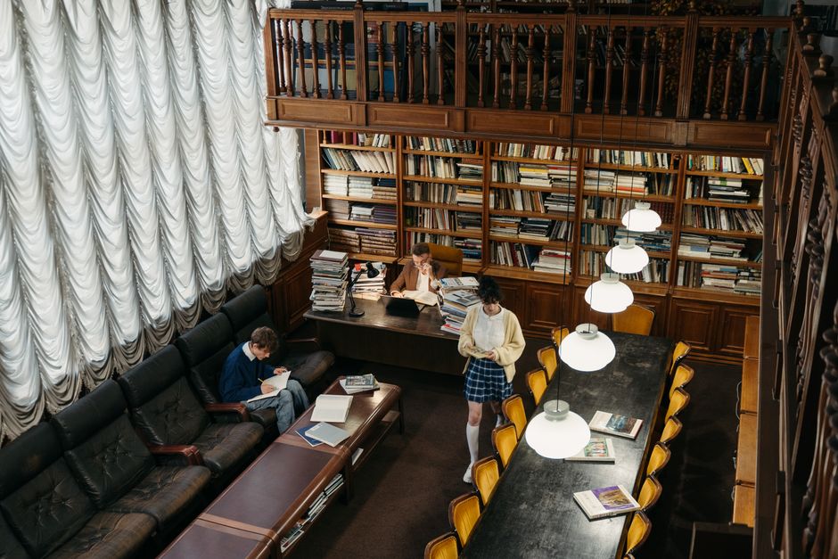 Two women studying in a quiet, well-lit library with spiral stairs and classic decor.